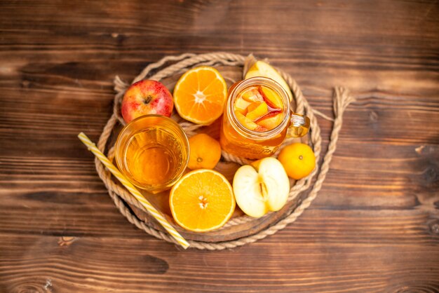 Vista aérea de jugo fresco orgánico en una botella y vaso servido con tubo y frutas sobre una tabla para cortar y sobre una mesa de madera marrón