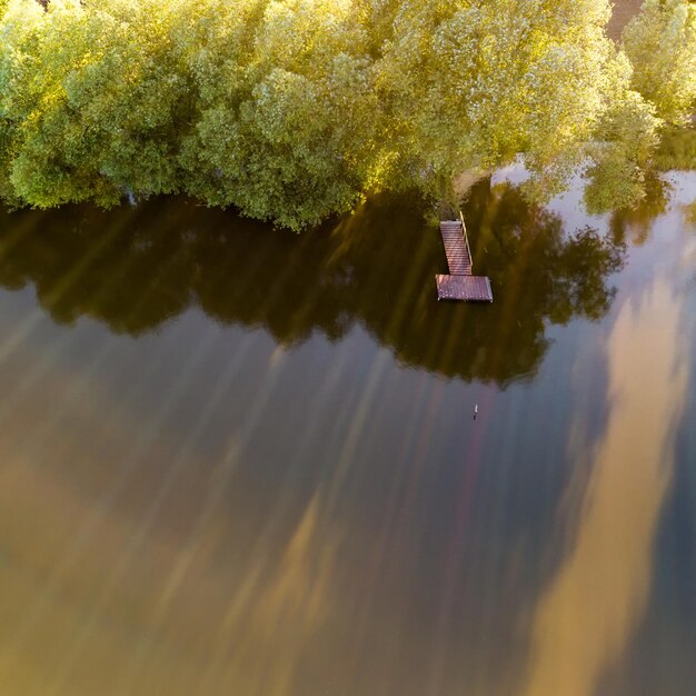 Vista aérea del lago con puente de madera para pescar rodeado de bosque Foto por drone