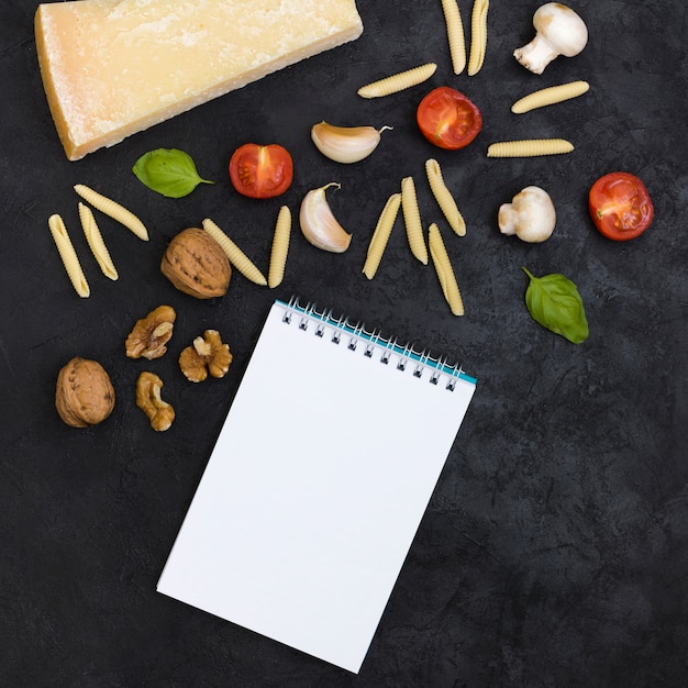 Foto gratuita vista aérea de la libreta espiral con ingredientes para hacer la pasta garganelli sobre fondo negro con textura