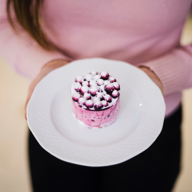 Una vista aérea de la mano de una mujer sosteniendo un delicioso pastel de arándanos en un plato de cerámica blanca