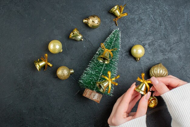 Vista aérea de la mano que sostiene las cajas de regalo de accesorios de decoración y el árbol de navidad sobre fondo oscuro