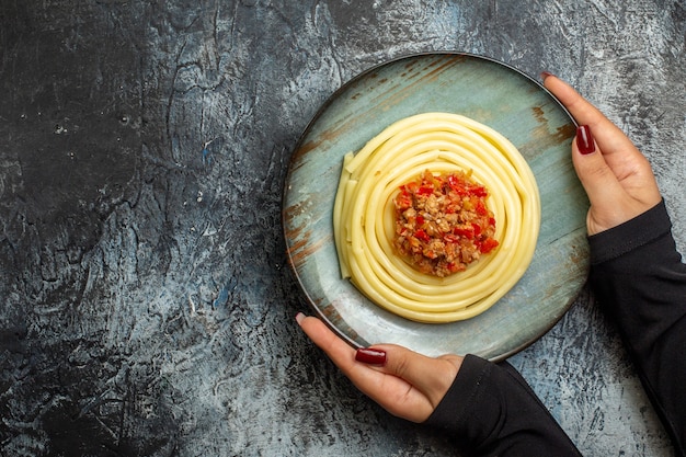 Vista aérea de la mano que sostiene la deliciosa pasta en un plato azul servido con tomate y carne para la cena en el lado izquierdo sobre fondo de hielo