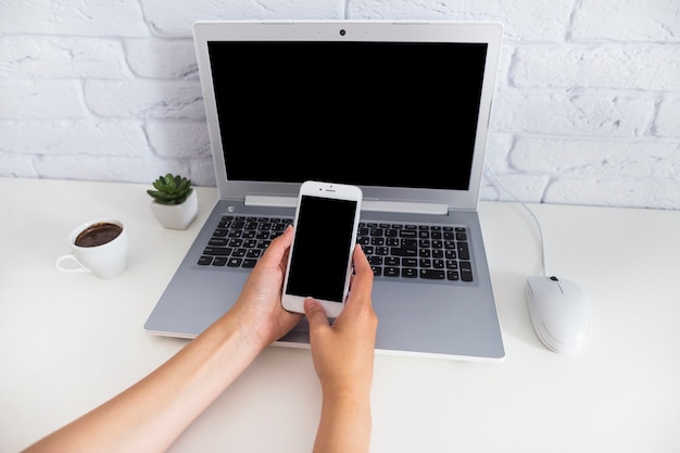 Vista aérea de la mano que sostiene el teléfono inteligente sobre la computadora portátil