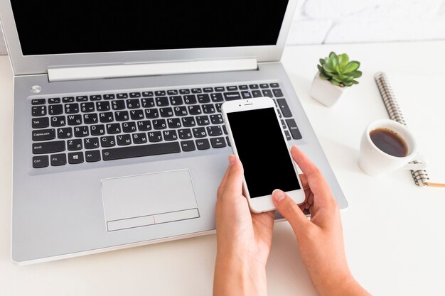 Vista aérea de la mano que sostiene el teléfono móvil sobre la computadora portátil