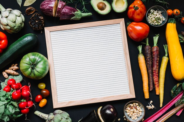 Una vista aérea del marco blanco de madera con verduras de colores sobre fondo negro