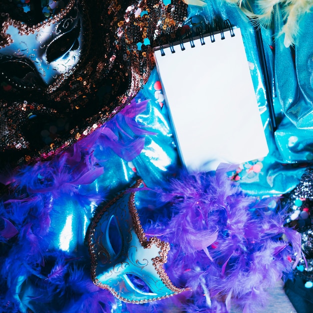 Vista aérea de máscara de ojo decorativa y objetos de carnaval con bloc de notas en espiral