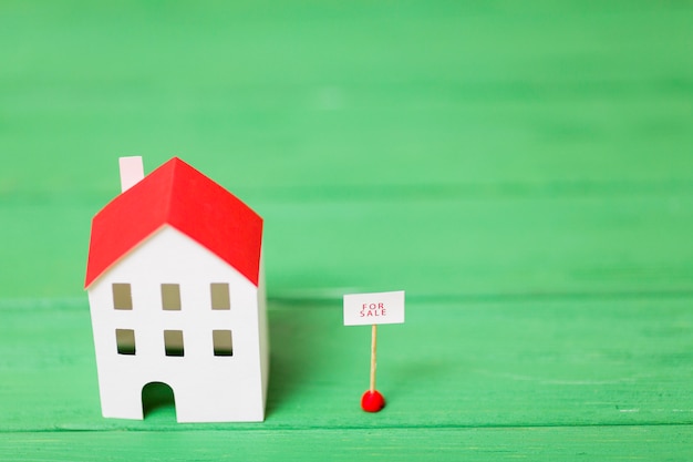 Una vista aérea del modelo de casa en miniatura cerca de la etiqueta de venta en el fondo con textura verde