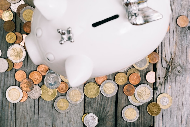 Una vista aérea de monedas alrededor del piggybank blanco en mesa de madera