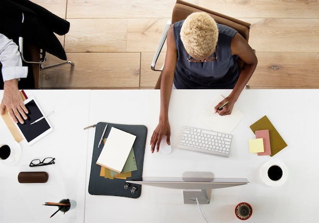 Vista aérea de la mujer de ascendencia africana que trabaja en la computadora en la mesa blanca en la oficina