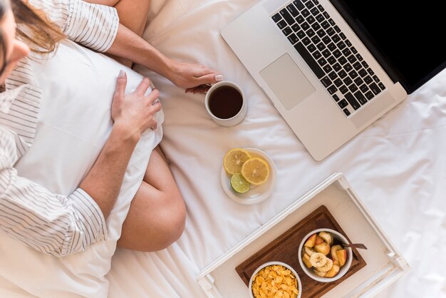 Una vista aérea de la mujer con desayuno y portátil en la cama