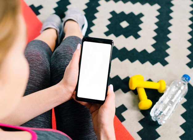 Una vista aérea de la mujer joven en forma que sostiene el teléfono móvil que muestra la pantalla en blanco en blanco