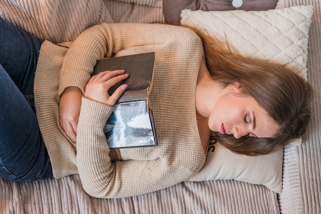 Una vista aérea de la mujer joven que duerme en cama con el libro en manos