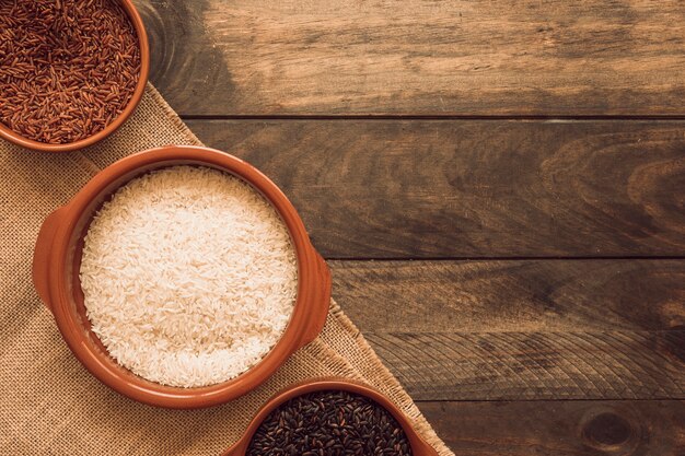 Vista aérea de negro; granos de arroz orgánicos rojos y blancos en tela de yute sobre la mesa de madera