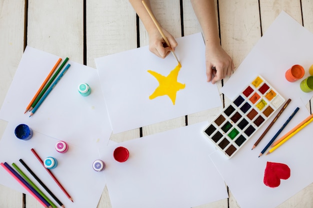 Foto gratuita una vista aérea de una niña pintando la estrella amarilla con pincel sobre papel blanco