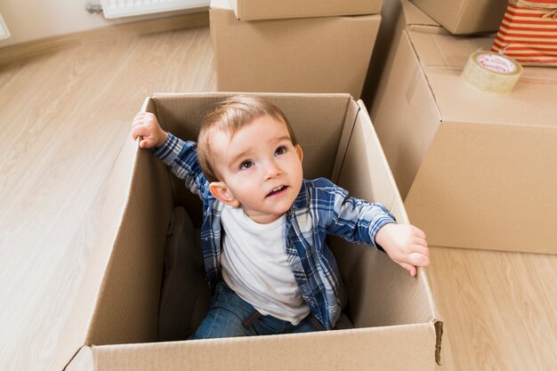 Una vista aérea de un niño pequeño sentado dentro de la caja de cartón mirando hacia arriba