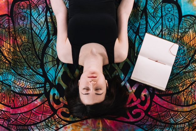 Vista aérea de los ojos cerrados mujer acostada cerca del libro en blanco abierto sobre la manta