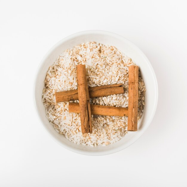 Una vista aérea de palitos de canela con un tazón de arroz crudo contra el fondo de madera