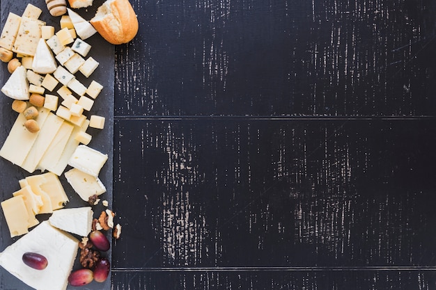 Una vista aérea de pan con diferentes tipos de queso con uvas sobre fondo negro con textura