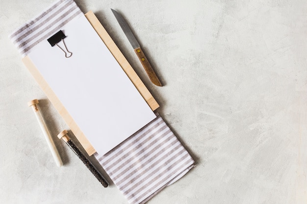 Una vista aérea de papel blanco en el portapapeles con un cuchillo; Servilletas y tubos de ensayo de especias.