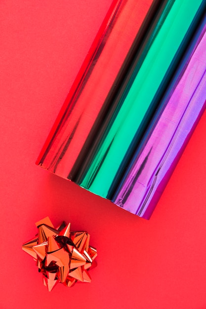 Vista aérea de papeles de regalo de brillo y arco sobre fondo rojo