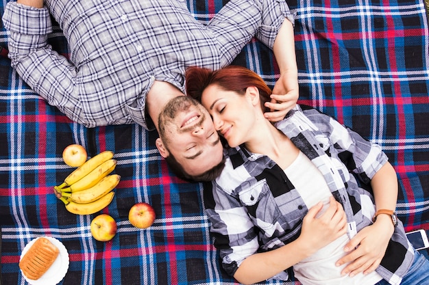 Una vista aérea de una pareja romántica sonriente sonriendo sobre una manta con frutas y hojaldre