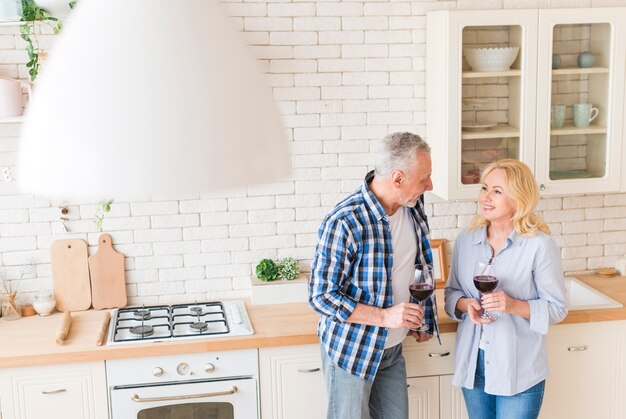 Una vista aérea de una pareja senior sosteniendo copas en mano de pie en la cocina