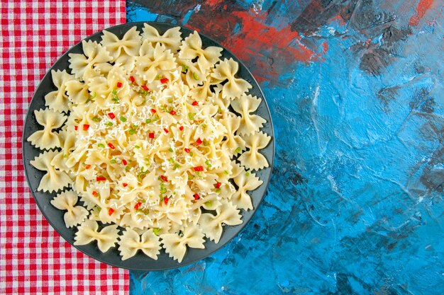 Vista aérea de la pasta farfalle italiana cruda con verduras en una toalla despojada de rojo sobre el cuadro azul