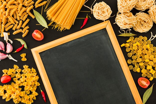 Una vista aérea de pastas crudas e ingredientes con pizarra pequeña en blanco