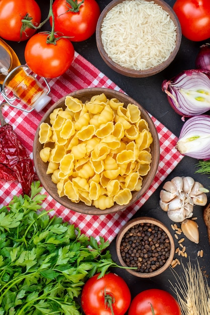 Vista aérea de pastas crudas en rojo toalla pelada verduras frescas rebanadas de pan botella de aceite caído un paquete verde sobre mesa negra