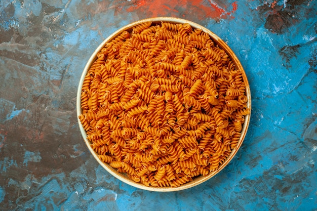 Vista aérea de pastas italianas crudas en un recipiente blanco sobre fondo azul.