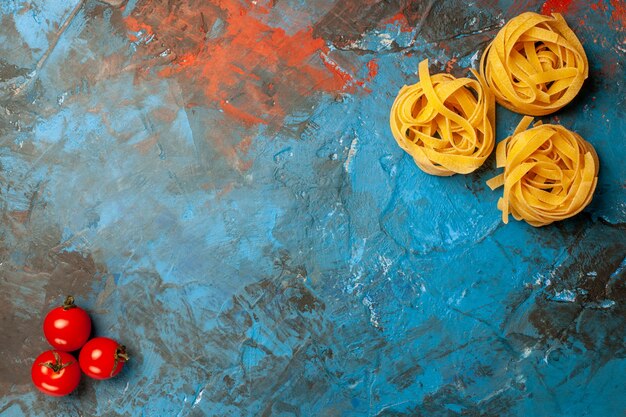 Vista aérea de pastas de tallarines y tomates sobre fondo azul.