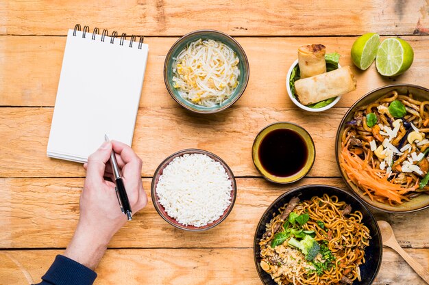 Una vista aérea de una persona que escribe en pluma con la libreta espiral con la comida tradicional tailandesa