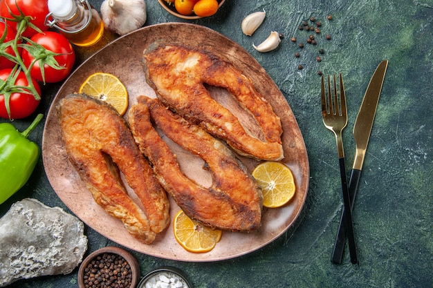 Vista aérea de pescados fritos y rodajas de limón en una placa marrón especias tomates aceite botella en mesa de mezcla de colores con espacio libre