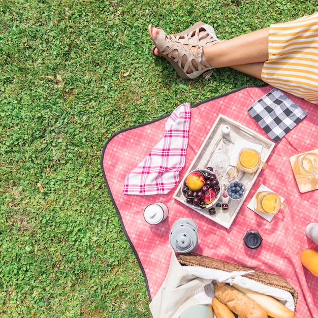 Vista aérea de la pierna de la mujer con desayuno en picnic sobre la hierba verde