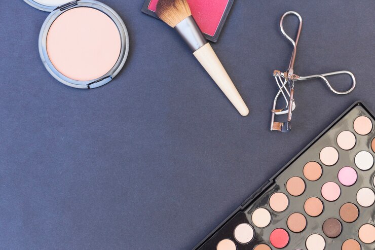 Foto gratuito una vista aérea del pincel de maquillaje; colorete; paleta de sombra de ojos y rizador de pestañas sobre fondo azul