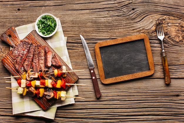 Vista aérea de un pincho de carne y bistec a la parrilla con pizarra en blanco