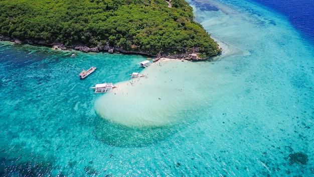 Vista aérea de la playa de arena con los turistas nadando en la hermosa agua de mar clara de la playa de la isla de Sumilon aterrizando cerca de Oslob, Cebú, Filipinas. - Aumentar el procesamiento de color.