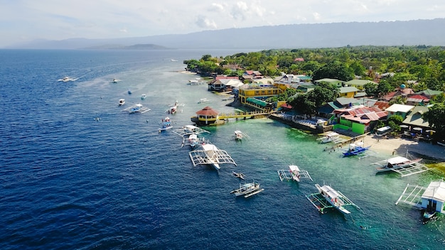 Vista aérea de la playa de arena con los turistas nadando en la hermosa agua de mar clara de la playa de la isla de Sumilon aterrizando cerca de Oslob, Cebú, Filipinas. - Aumentar el procesamiento de color.