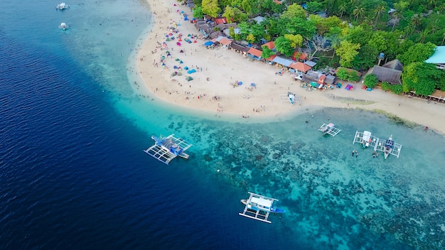 Vista aérea de la playa de arena con los turistas nadando en la hermosa agua de mar claro de la playa de la isla de Sumilon aterrizando cerca de Oslob, Cebú, Filipinas. - Aumentar el procesamiento de color.