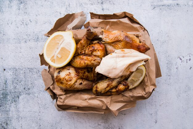 Vista aérea de pollo hervido y asado con limón en papel marrón sobre fondo de concreto