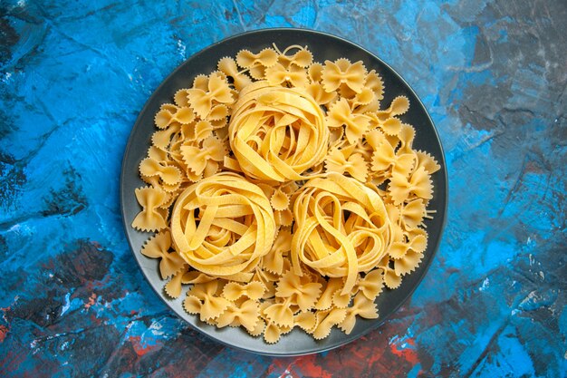 Vista aérea de la preparación de la cena con fideos de pasta en una placa negra sobre fondo azul.