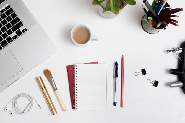 Vista aérea de productos cosméticos; Material de oficina; Taza de café y portátil con planta en escritorio de oficina