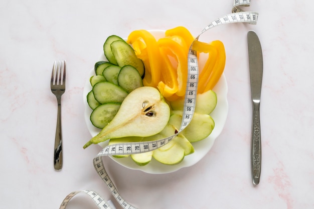 Vista aérea de rebanadas orgánicas de vegetales y frutas en un plato con cinta métrica