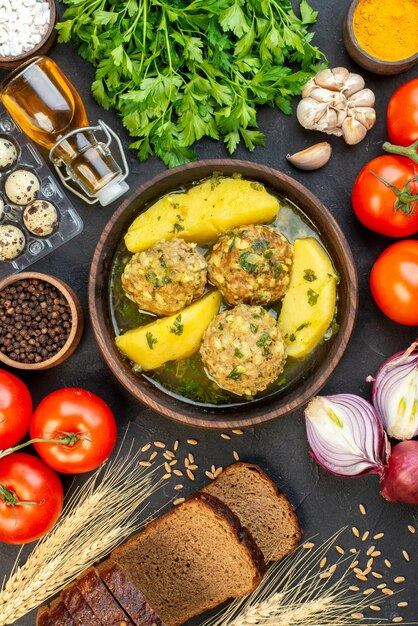 Vista aérea de rebanadas de pan negro deliciosa comida de albóndigas con patatas verdes y verduras frescas sobre fondo negro