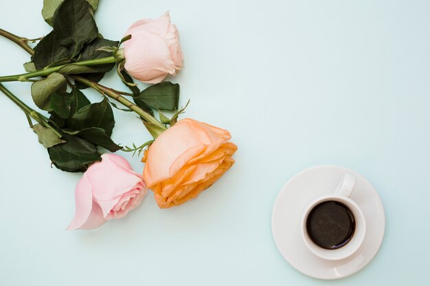 Una vista aérea de rosas coloridas con taza de café y platillo sobre fondo azul