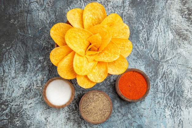 Vista aérea de sabrosas patatas fritas decoradas con forma de flor y diferentes especias en mesa gris