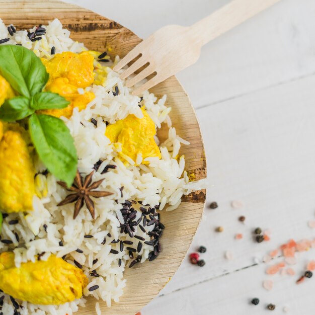 Vista aérea de sabroso pollo y arroz en un plato con hojas de albahaca