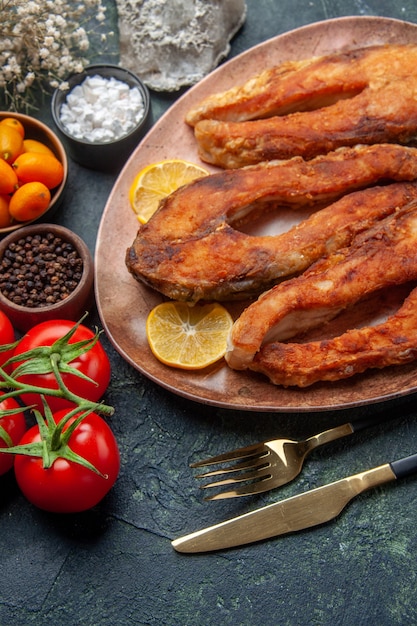 Vista aérea de sabrosos pescados fritos y rodajas de limón en una placa marrón tomates kumquats en mesa de mezcla de colores con espacio libre