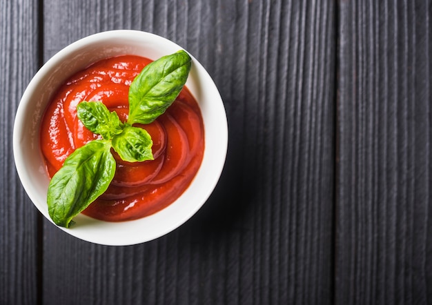 Foto gratuita una vista aérea de salsa de tomate con hojas de albahaca verde sobre fondo de madera