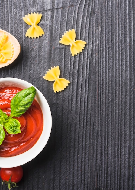 Foto gratuita una vista aérea de salsa de tomate con pasta sin cocer sobre fondo negro de madera